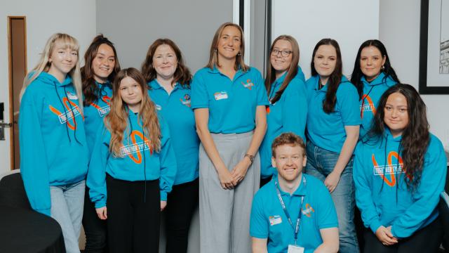 In this image, the North of England youth team can be seen posing for a photo. The photo shows them from the waist up and shows an inflatable play area in the background. They are both wearing pale blue Diabetes UK t-shirts and the boy is wearing a navy blue Diabetes UK hoodie. The girl on the left has brown hair, past her shoulders. The boy on the right has short dark hair and a well groomed beard. 