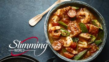 Reddish seafood curry with green chillies and spinach in a stone bowl on slate