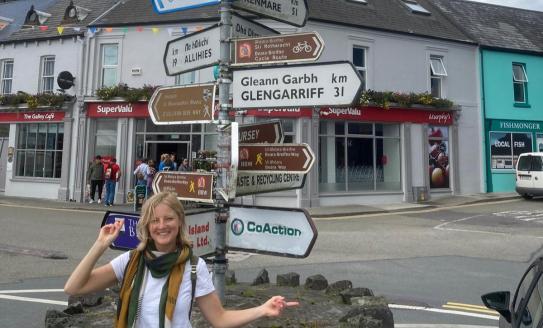 Lucy wears a white t-shirt, standing at a crossroads 
