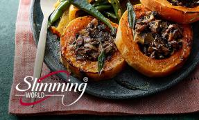 Baked squash rings filled with fried mushrooms and onions, decorated with sage leaves. The meal is on a stone plate with a side of roasted green and yellow bell peppers and a wooden spoon.