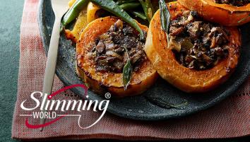 Baked squash rings filled with fried mushrooms and onions, decorated with sage leaves. The meal is on a stone plate with a side of roasted green and yellow bell peppers and a wooden spoon.
